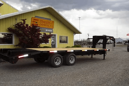 Flatbed trailer parked beside a yellow warehouse on a gravel lot under cloudy skies