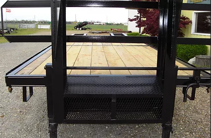 Black metal trailer with wooden floor and railings on a gravel path in a park-like setting