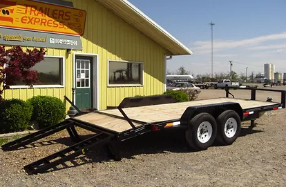 Black flatbed trailer parked outside a yellow building in a gravel lot.