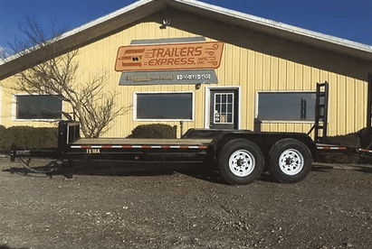 Black utility trailer parked in front of a yellow trailer sales building