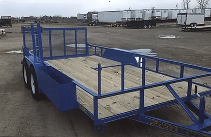 Blue flatbed utility trailer parked in an open lot with white trucks in the background