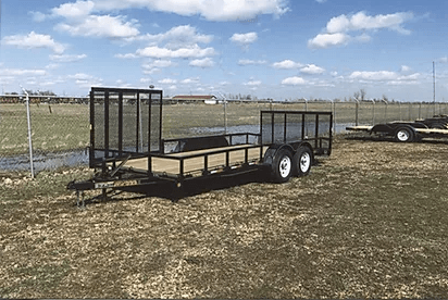 Black utility trailer with mesh gates parked on a grassy field under a cloudy blue sky.