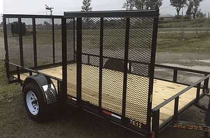 Black utility trailer with mesh sides and wooden floor on a gravel lot