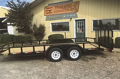 Black utility trailer parked outside a yellow trailers shop with a sign reading “Trailers Express”