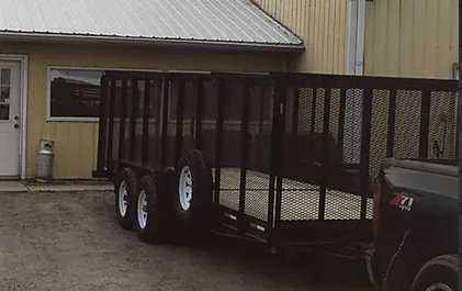 Black enclosed utility trailer parked beside a beige building on wet pavement.