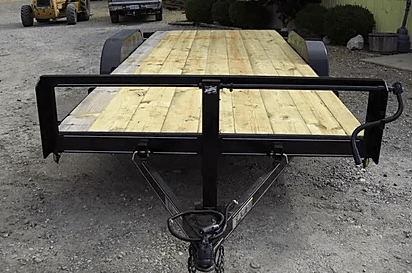 Wooden flatbed trailer with black metal frame parked on gravel