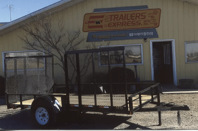 Trailer parked outside a trailer sales office with a tan building and sign in the background
