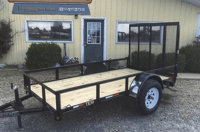 Black utility trailer with wood sides parked outside a beige building