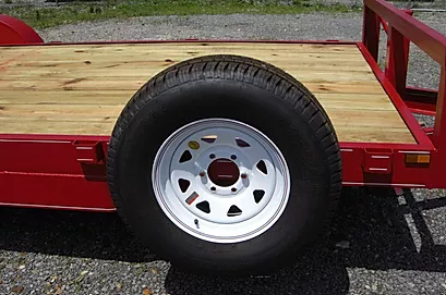 Close-up of a trailer wheel with a white rim and black tire beside a red flatbed trailer deck