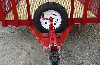 Red trailer hitch with a mounted spare tire and black coupler on gravel