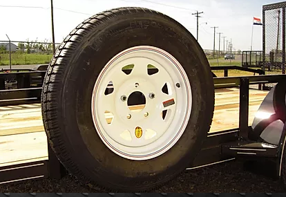 White spare tire mounted on a trailer, with a road and utility poles in the background