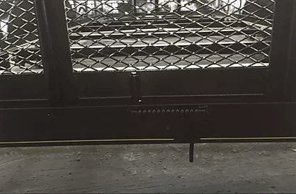 Black metal gate with a diamond lattice pattern across a concrete floor indoors.