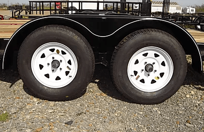 Two white trailer wheels with black tires on a black utility trailer over gravel