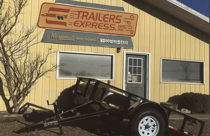 Damaged black trailer crashed into a yellow building with a “Trailers Express” sign.