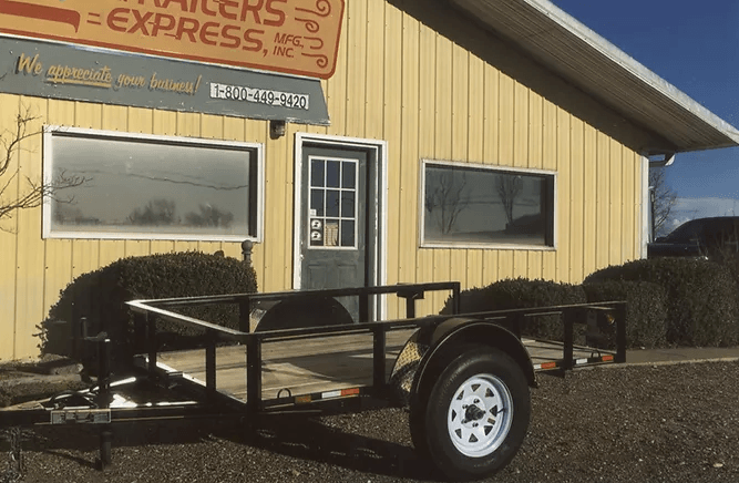 Black utility trailer parked outside a yellow building with an Express sign.