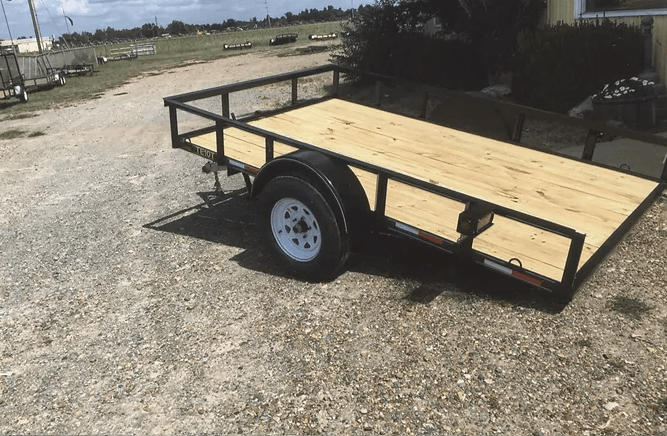 Small utility trailer with wooden deck parked on a gravel lot outdoors