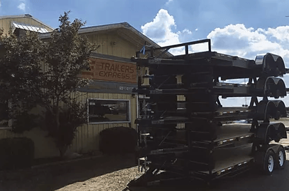 Stacked black canoes on a trailer outside a building under a cloudy sky