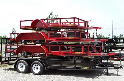 Red trailer stacked with multiple red metal carts parked outdoors on gravel