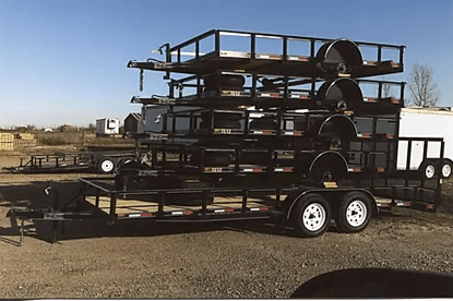 Stacked metal trailer frames on a flatbed trailer in an outdoor lot.