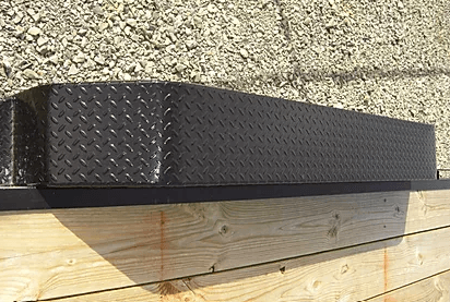 Black diamond-plate metal edge flashing on a wooden wall beneath rough stucco siding