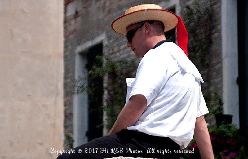 A man wearing a straw hat and sunglasses is sitting in front of a building.