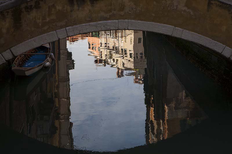 A boat is reflected in a puddle of water under a bridge.