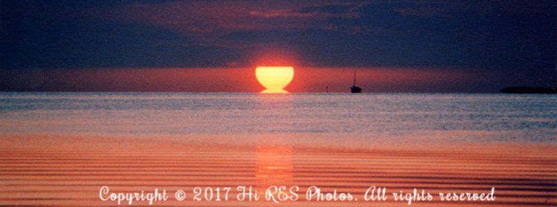 The sun is setting over the ocean with a boat in the distance.