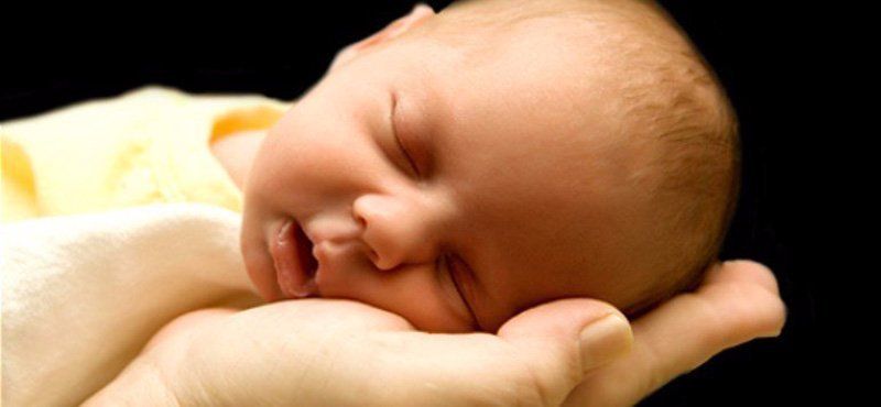 A person is holding a sleeping baby in their hands.