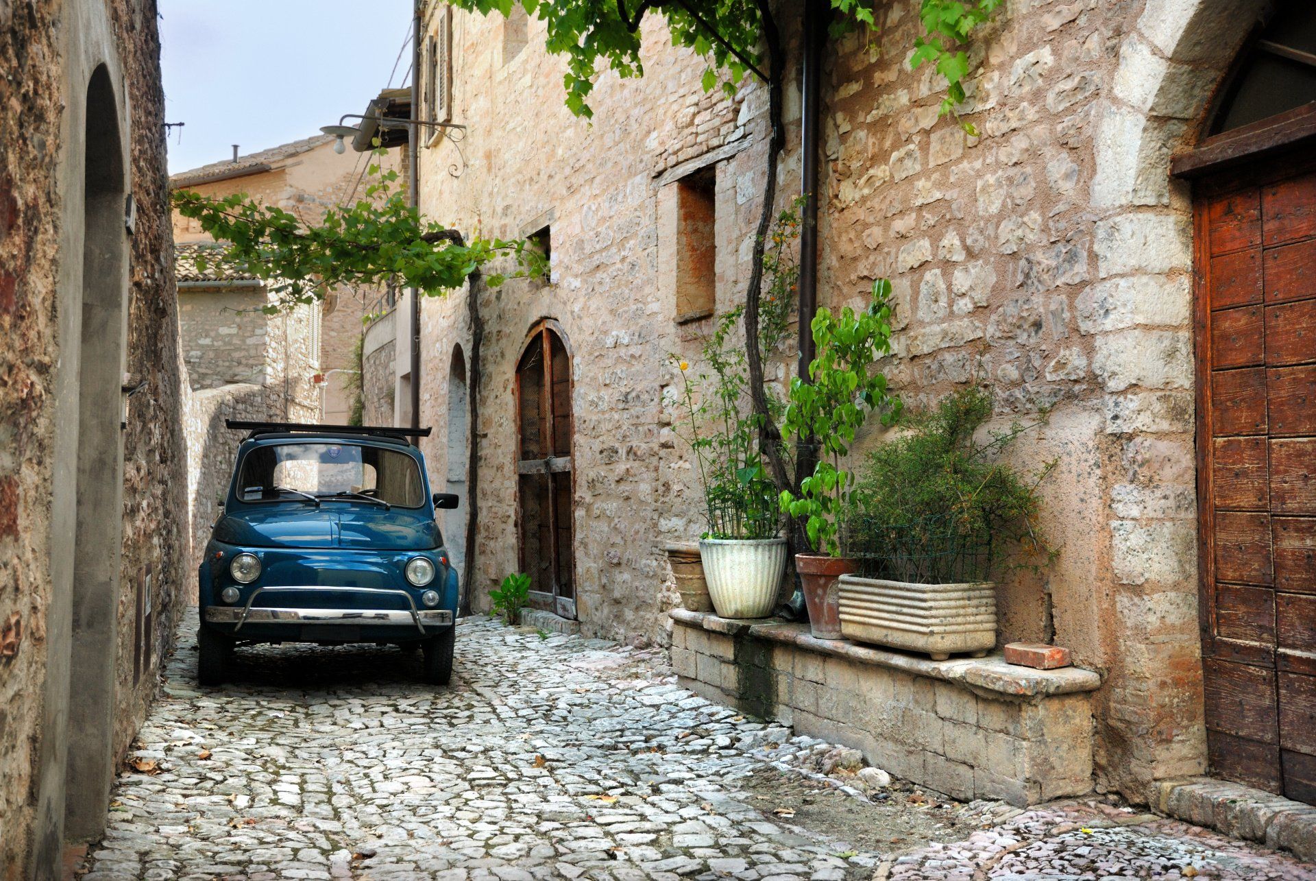 A blue car is parked in the middle of a cobblestone street.