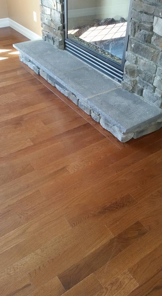 A wooden floor next to a stone fireplace in a living room.