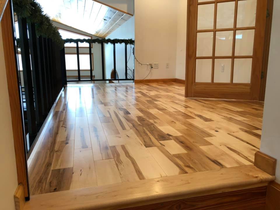 A wooden floor in a room with stairs and a sliding glass door.