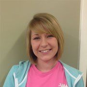 A woman wearing a pink shirt and a blue hoodie is smiling.
