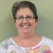 A woman wearing glasses and a necklace is smiling for the camera.