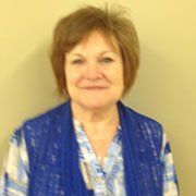 A woman wearing a blue vest and a plaid shirt is smiling for the camera.