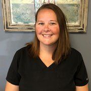A woman in a black scrub top is smiling in front of a framed picture.