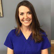 A woman in a blue scrub top is smiling for the camera.