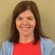 A woman wearing a red shirt and a blue sweater is smiling for the camera.