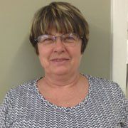 A woman wearing glasses and a blue and white shirt is smiling for the camera.