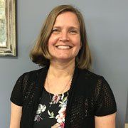 A woman wearing a black cardigan and a floral shirt is smiling for the camera.