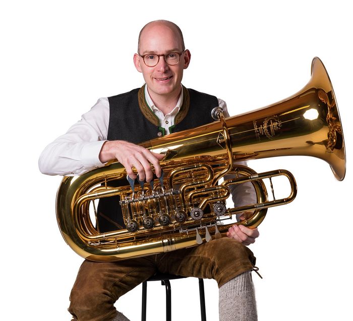 Ein Mann sitzt auf einem Hocker und hält eine Tuba.