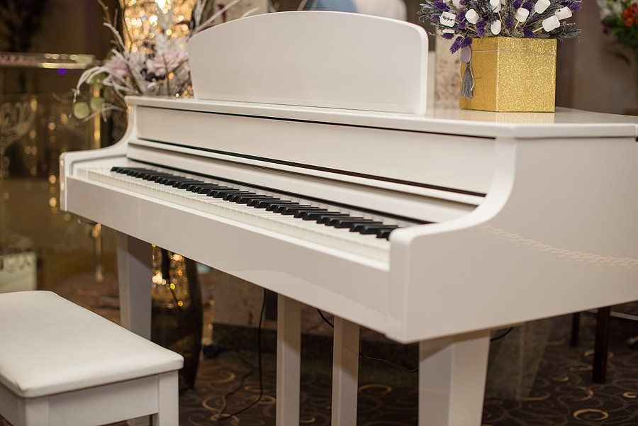 White piano with matching bench in a decorative setting, featuring a gold square vase and floral arrangement.