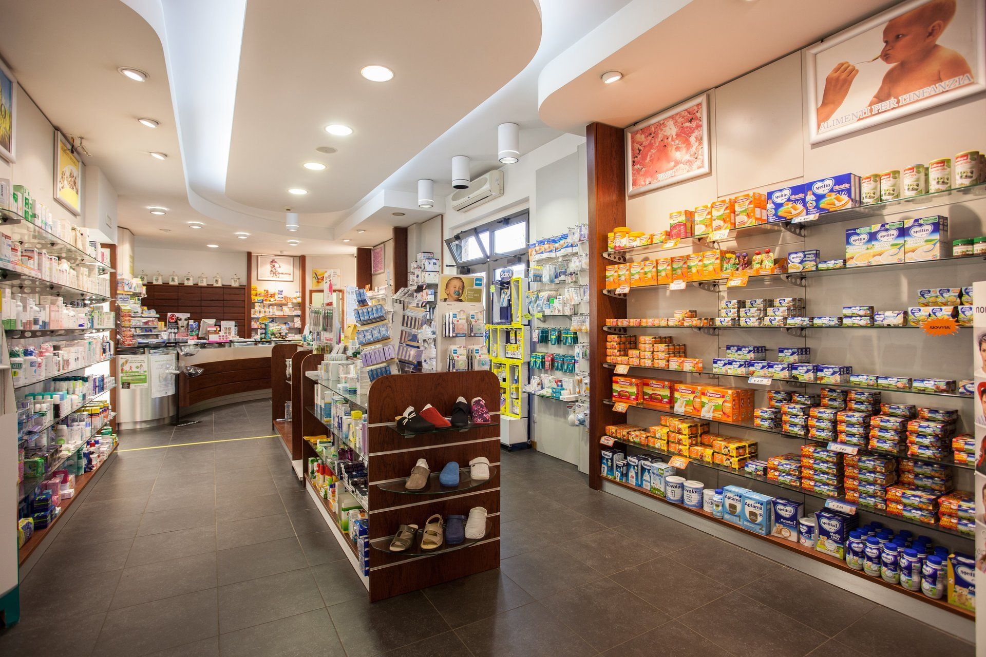 L'interno di una farmacia ben illuminata, con scaffali bianchi pieni di vari prodotti per la salute e il benessere.