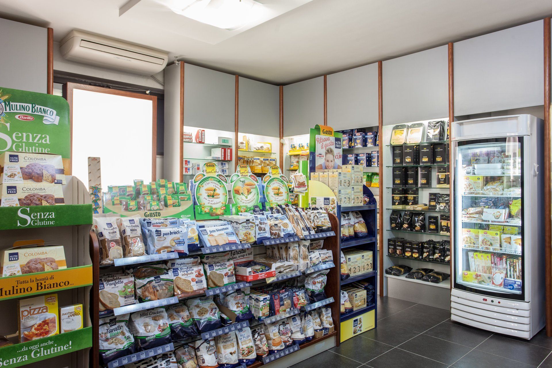 Scaffali pieni di prodotti alimentari confezionati e un'alta vetrina refrigerata in un negozio ben illuminato.