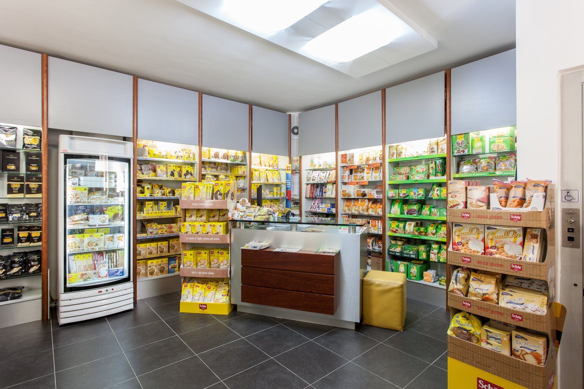 Interno di un negozio con scaffali pieni di vari prodotti alimentari confezionati, un frigorifero e una cassa centrale.