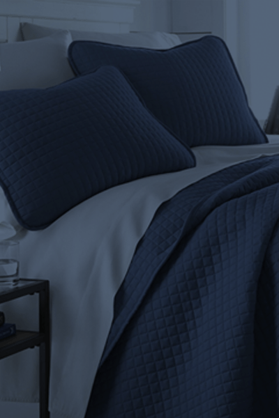 Sábanas y almohadas de color azul oscuro sobre una cama sin hacer en un dormitorio con iluminación tenue.