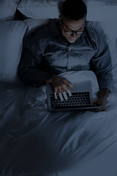 Persona usando una computadora portátil en la cama bajo una iluminación azul tenue.