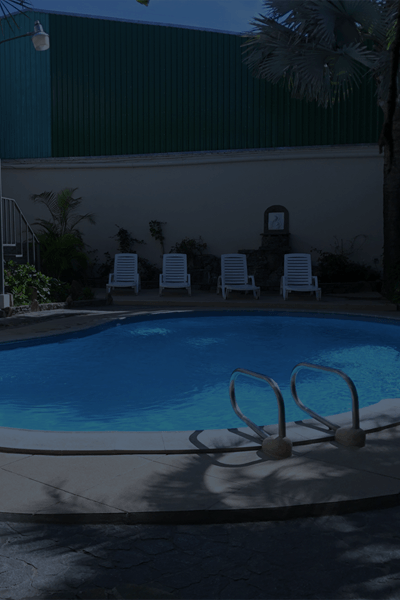 Piscina de agua azul, tumbonas y una escalera metálica en un patio sombreado.