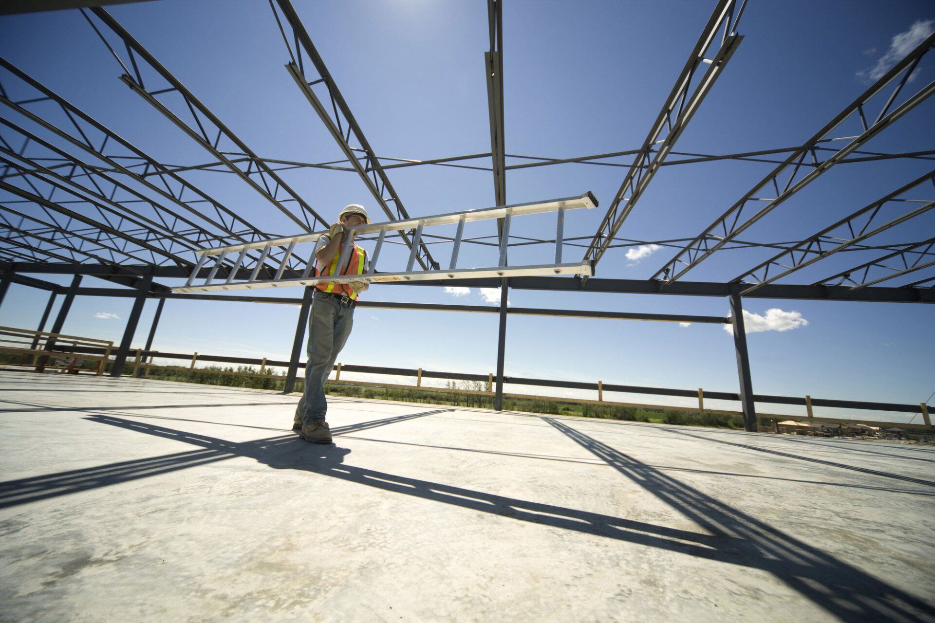 Worker carrying a ladder under a Steel structure