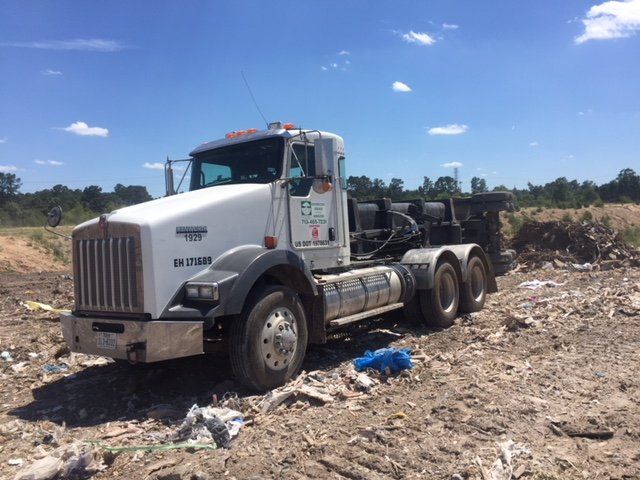 White Kenworth dump truck in a landfill on a sunny day.