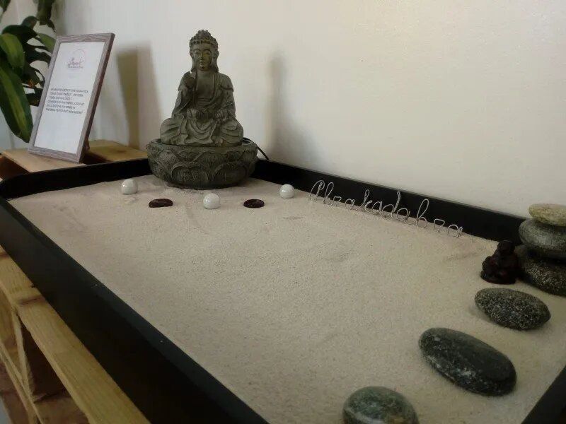 Giardino zen di sabbia con statua di Buddha, sabbia rastrellata, ciottoli e bordo nero su un tavolo